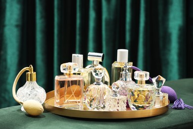 Photo of Different luxury perfumes on green pouf near teal curtains