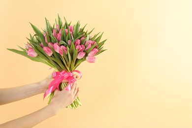 Photo of Woman with bouquet of beautiful tulips on beige background, closeup. Space for text