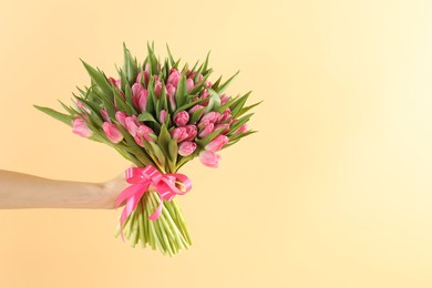 Photo of Woman with bouquet of beautiful tulips on beige background, closeup. Space for text