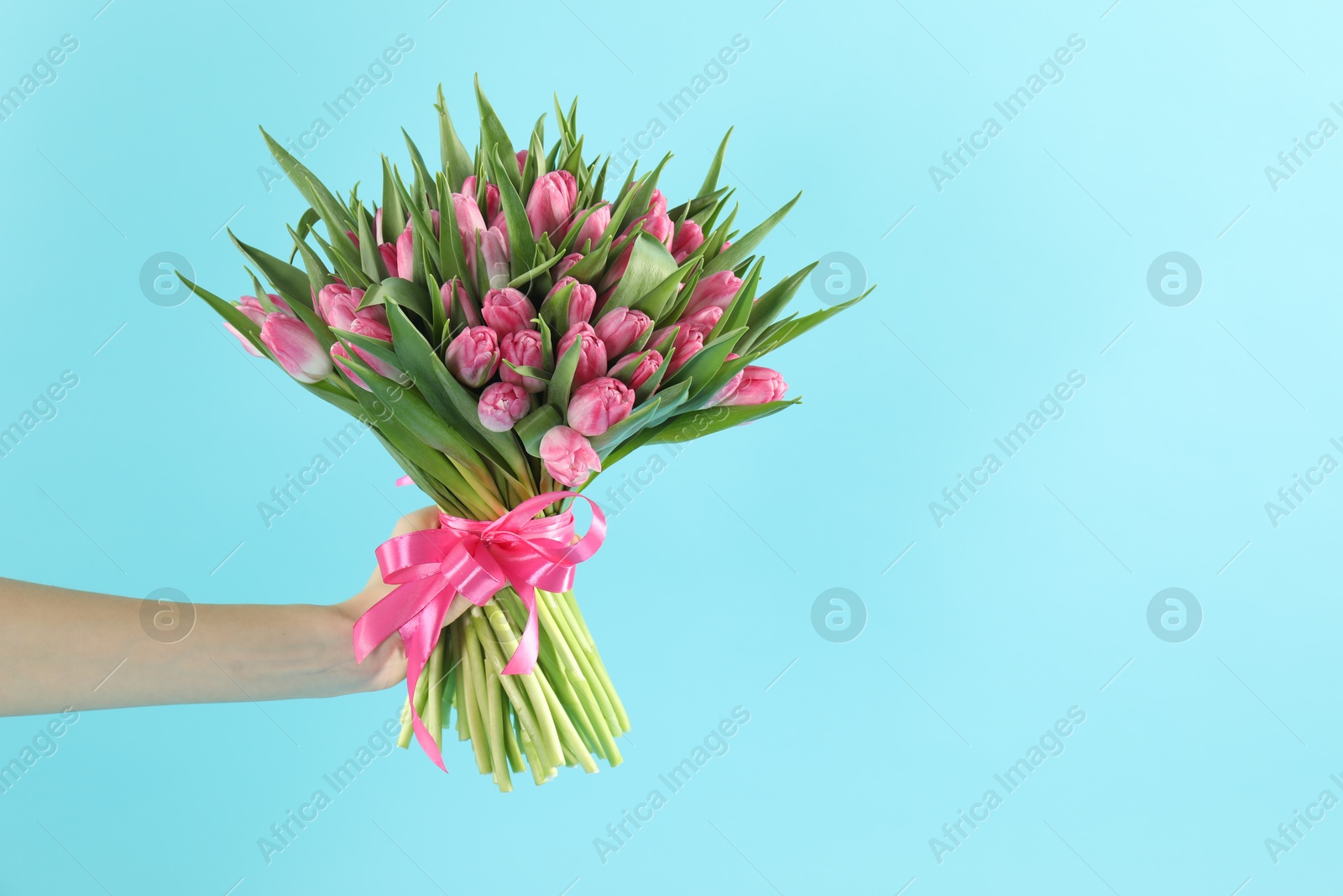 Photo of Woman with bouquet of beautiful tulips on light blue background, closeup. Space for text