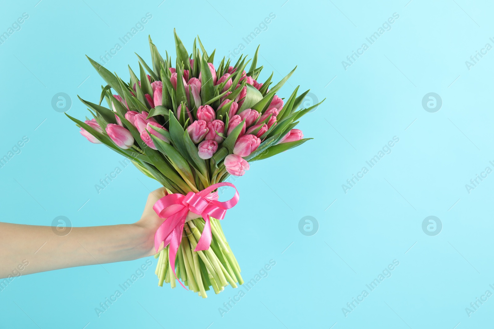 Photo of Woman with bouquet of beautiful tulips on light blue background, closeup. Space for text