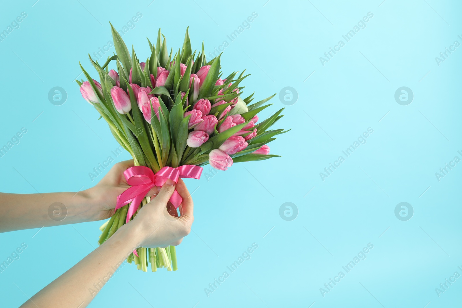 Photo of Woman with bouquet of beautiful tulips on light blue background, closeup. Space for text