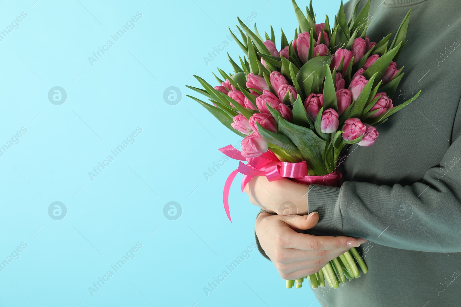 Photo of Woman with bouquet of beautiful tulips on light blue background, closeup. Space for text