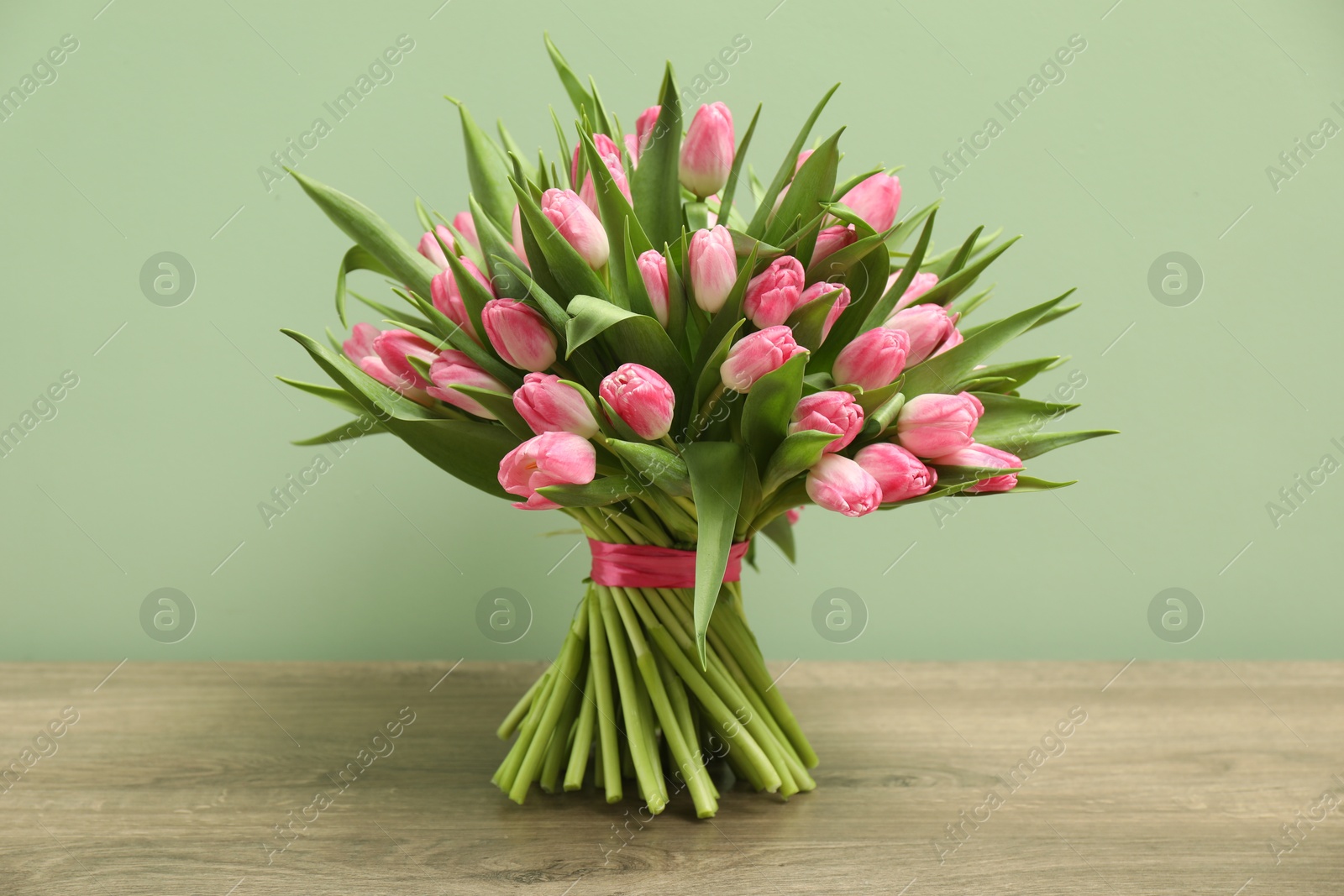 Photo of Bouquet of beautiful tulips on wooden table against pale green background