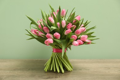 Bouquet of beautiful tulips on wooden table against pale green background