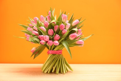 Photo of Bouquet of beautiful tulips on wooden table against orange background