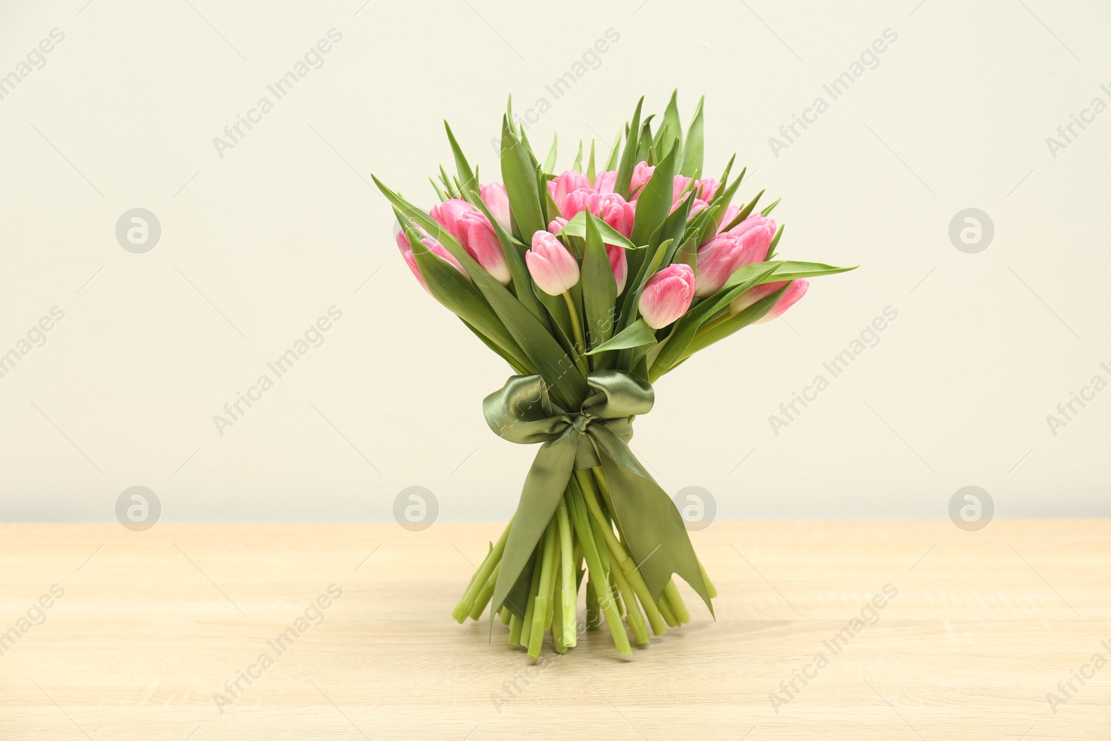 Photo of Bouquet of beautiful tulips on wooden table against light grey background