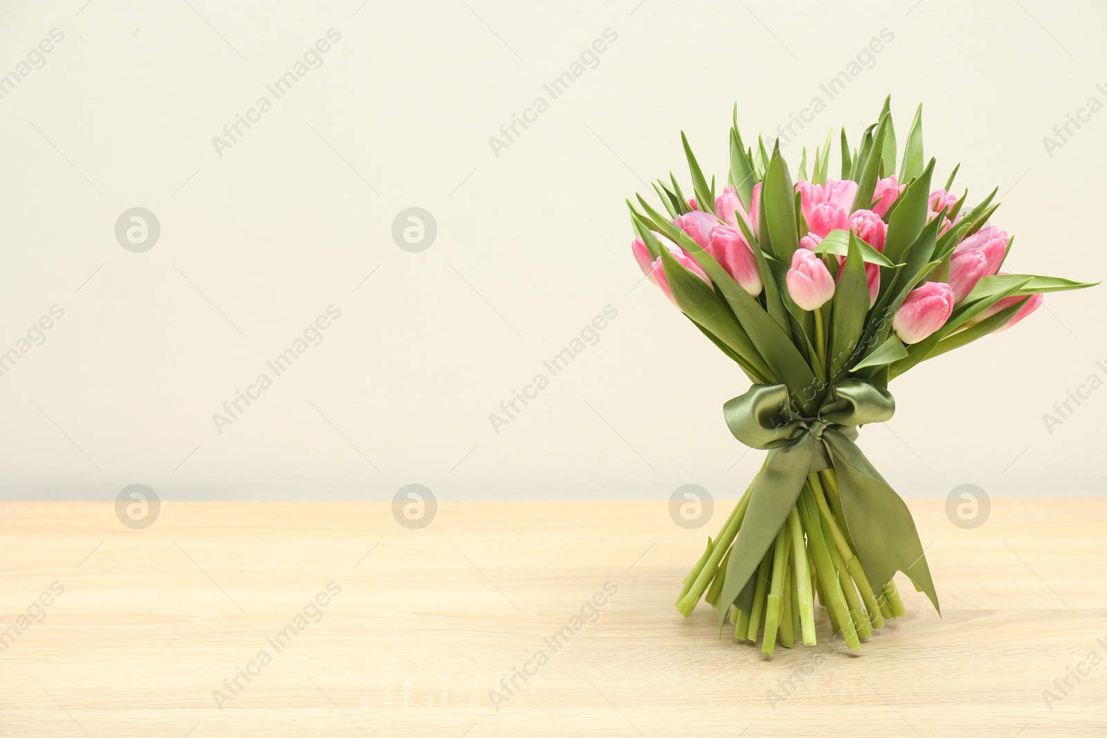 Photo of Bouquet of beautiful tulips on wooden table against light grey background, space for text