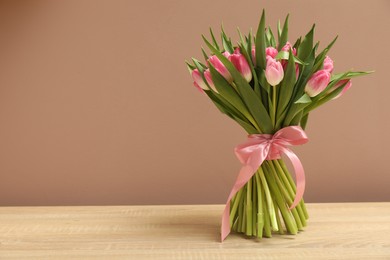 Bouquet of beautiful tulips on wooden table against dark beige background, space for text