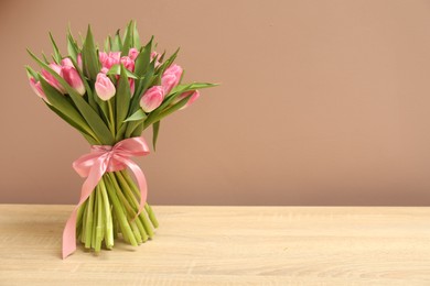 Photo of Bouquet of beautiful tulips on wooden table against dark beige background, space for text