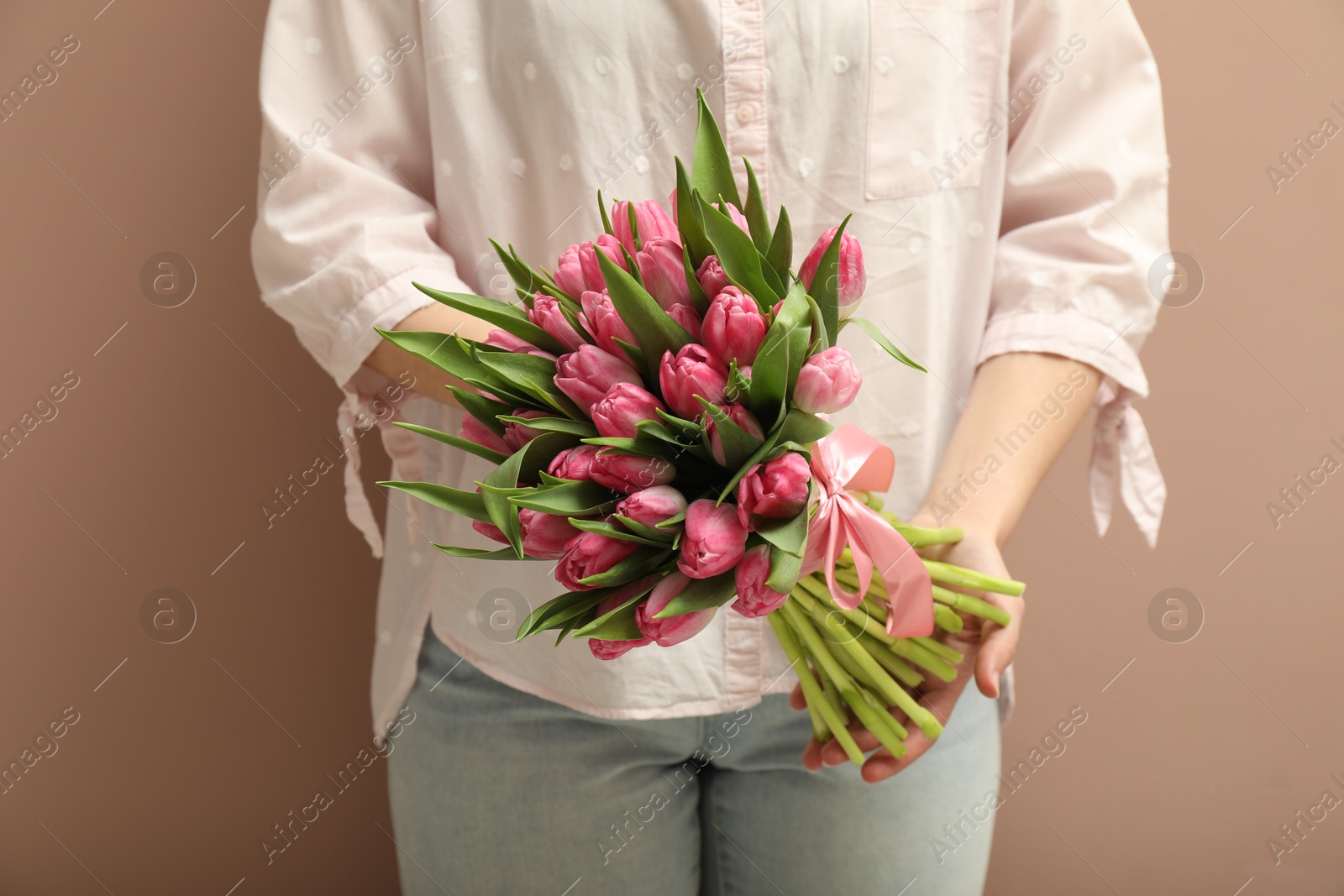 Photo of Woman with bouquet of beautiful tulips on dark beige background, closeup