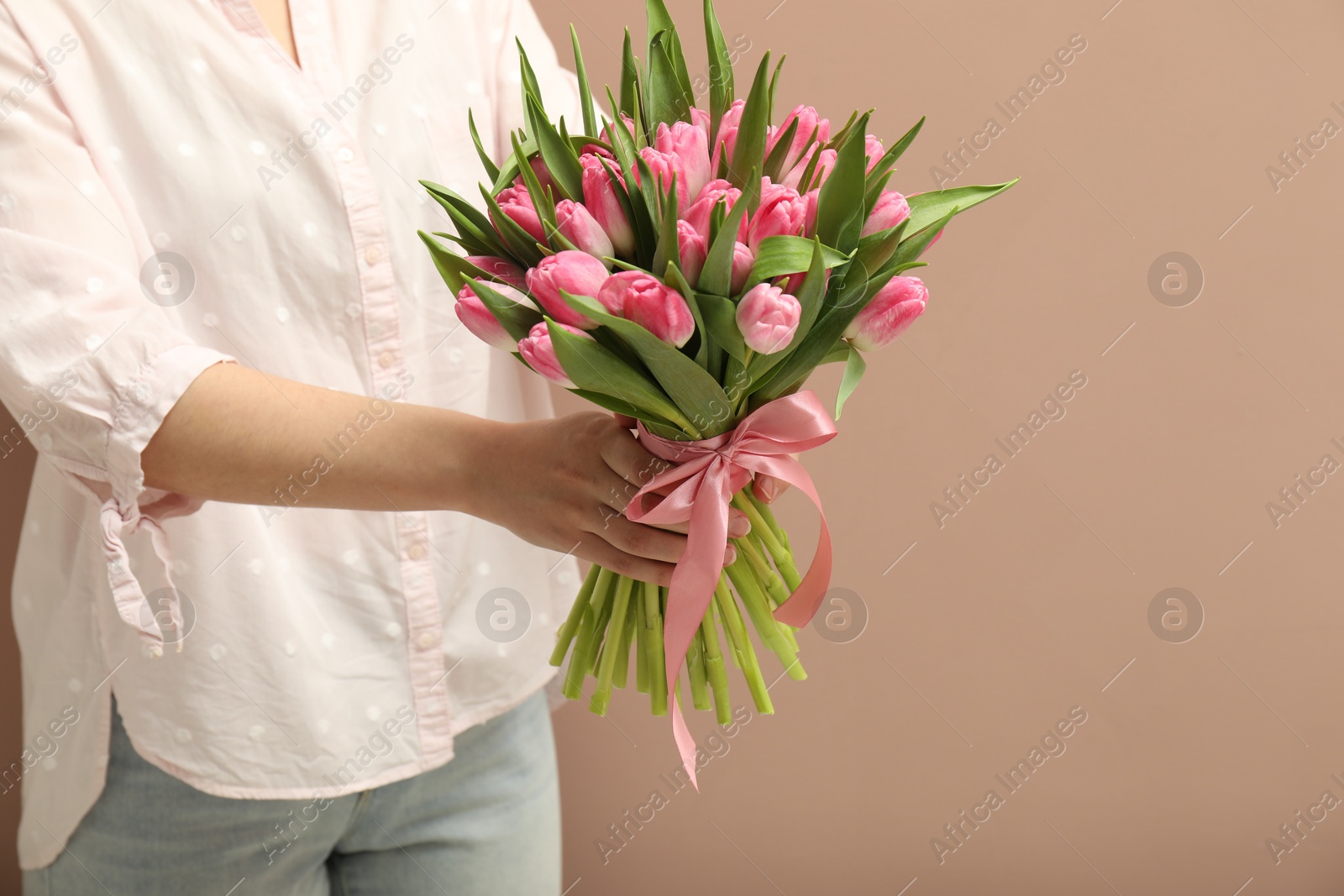 Photo of Woman with bouquet of beautiful tulips on dark beige background, closeup. Space for text