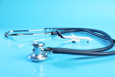 Photo of Stethoscope and airplane model on light blue background, closeup