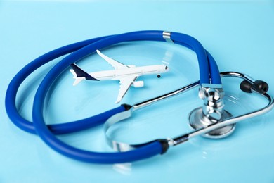 Photo of Stethoscope and airplane model on light blue background, closeup