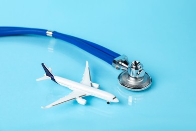 Photo of Stethoscope and airplane model on light blue background, closeup