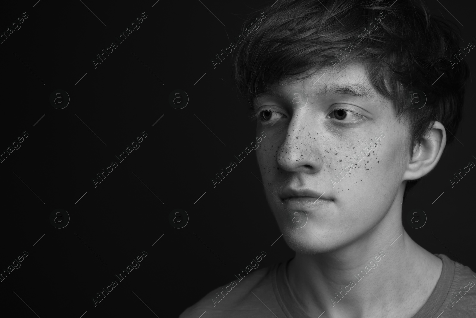 Photo of Teenage boy with freckles on dark background, black and white effect. Space for text