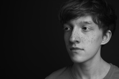 Photo of Teenage boy with freckles on dark background, black and white effect. Space for text