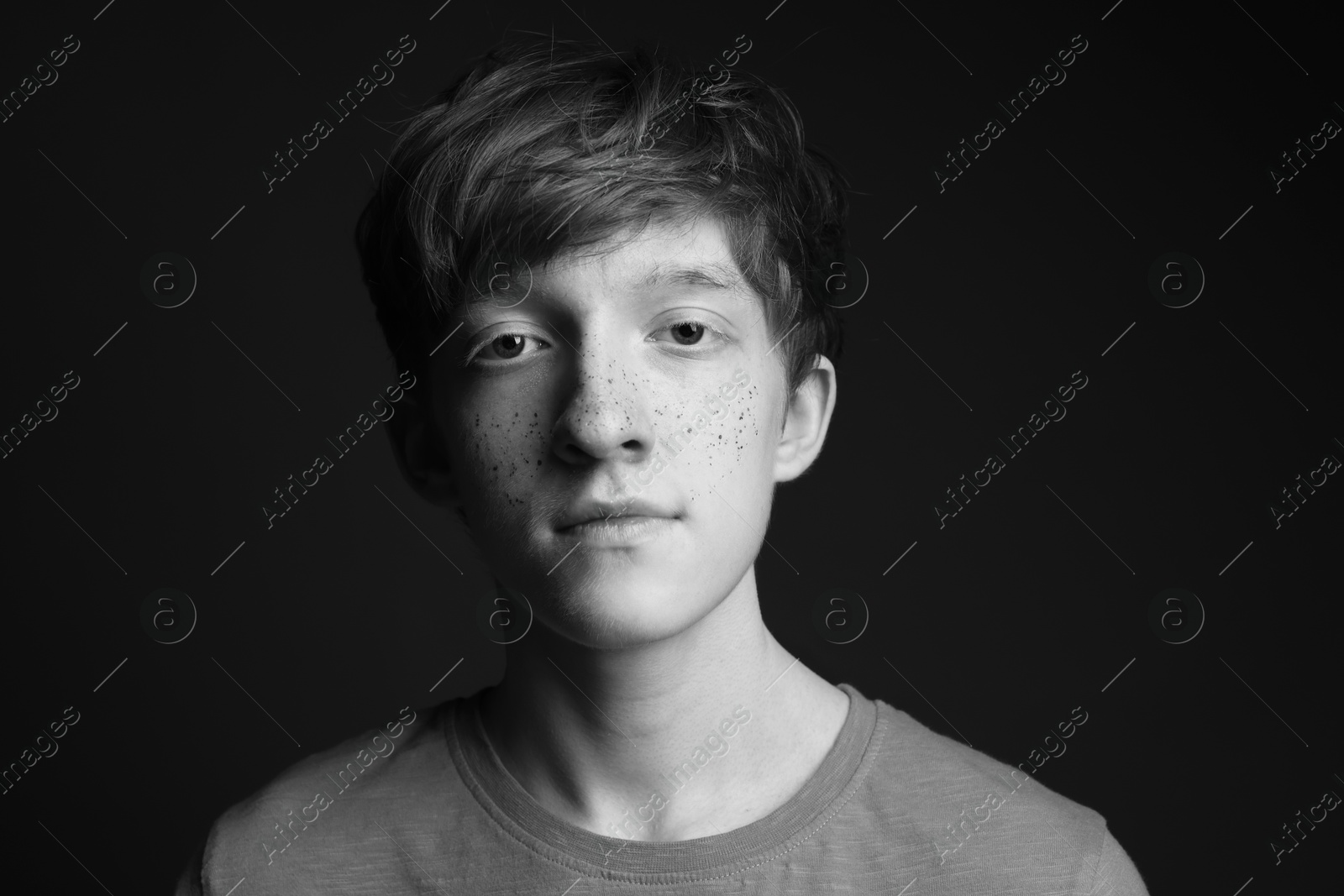 Photo of Teenage boy with freckles on dark background, black and white effect