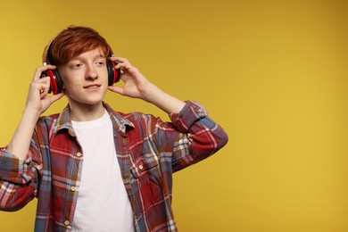 Smiling teenage boy with freckles listening to music by headphones on yellow background. Space for text