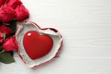 Photo of Heart shaped chocolate in box and red roses on white wooden table, flat lay. Space for text