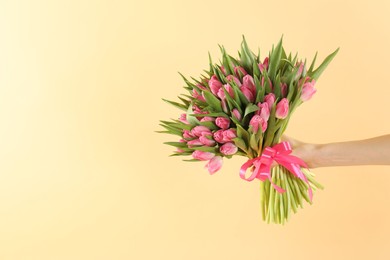 Photo of Woman with bouquet of beautiful tulips on beige background, closeup. Space for text