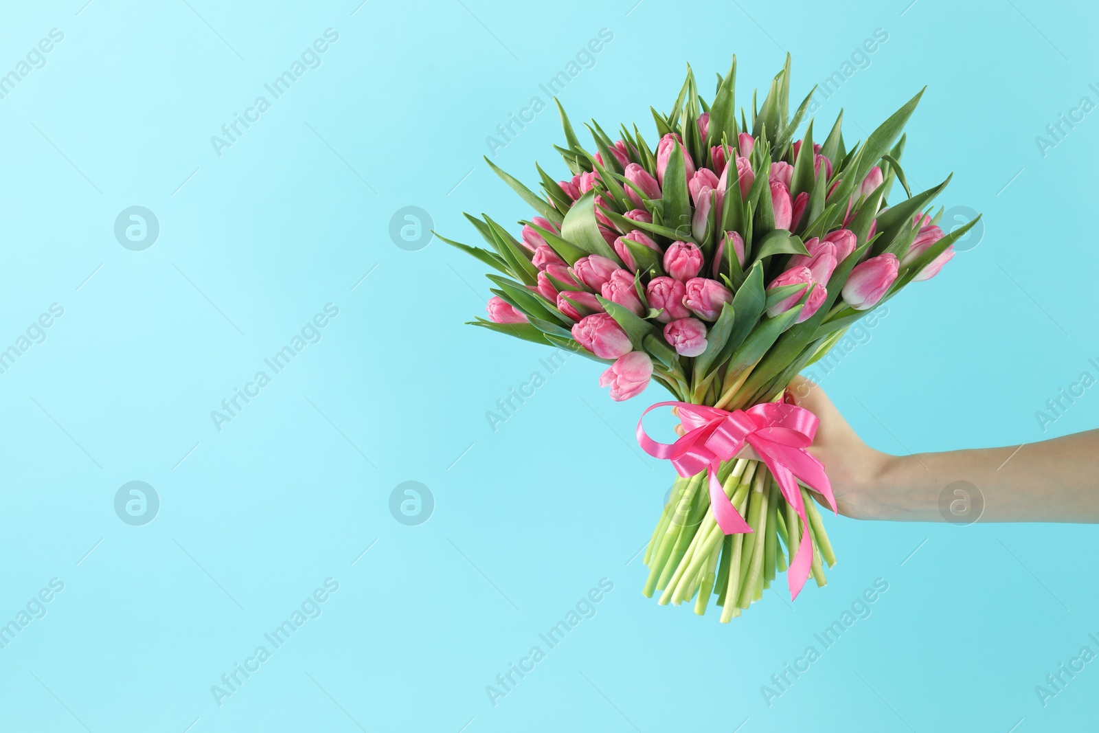 Photo of Woman with bouquet of beautiful tulips on light blue background, closeup. Space for text