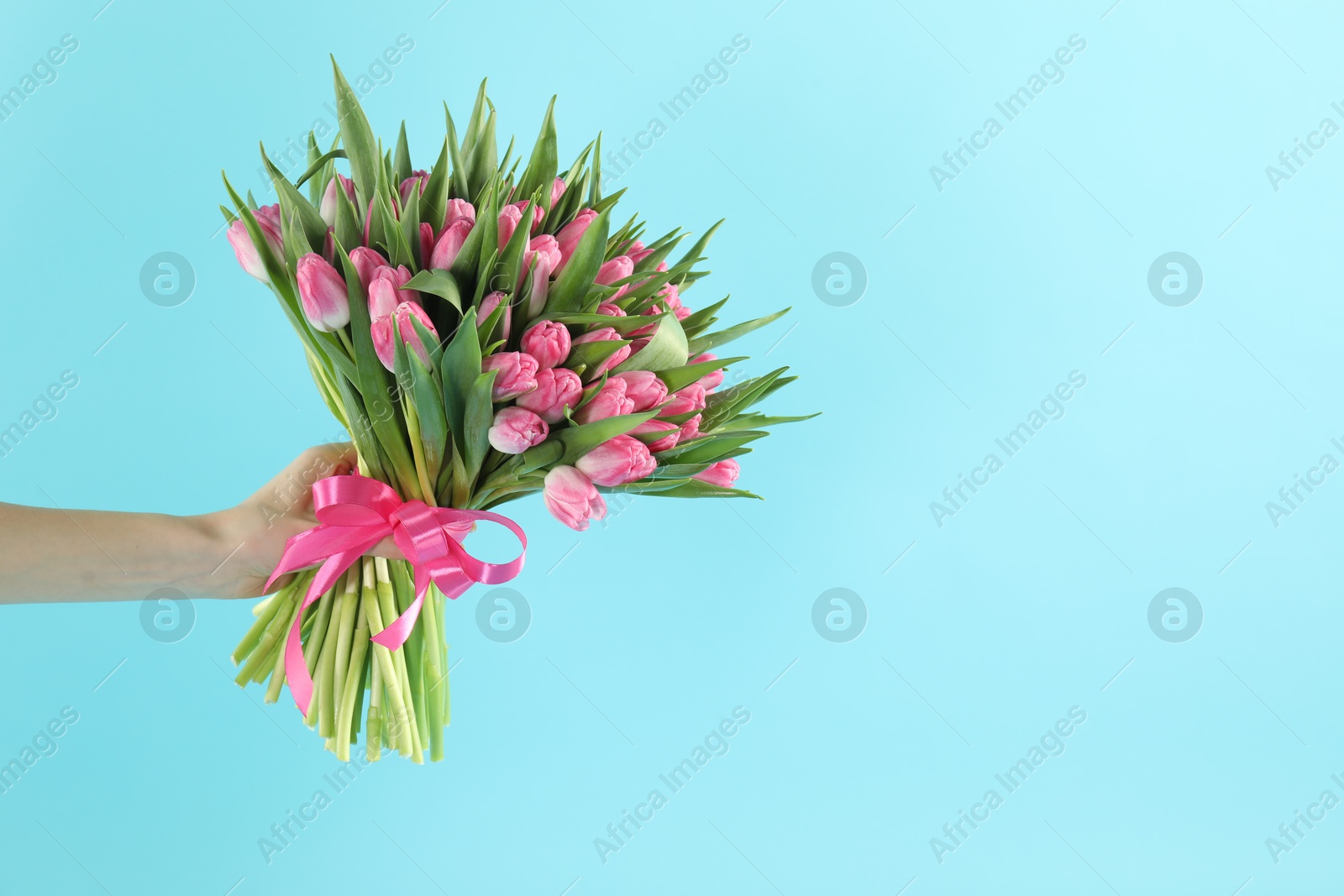 Photo of Woman with bouquet of beautiful tulips on light blue background, closeup. Space for text