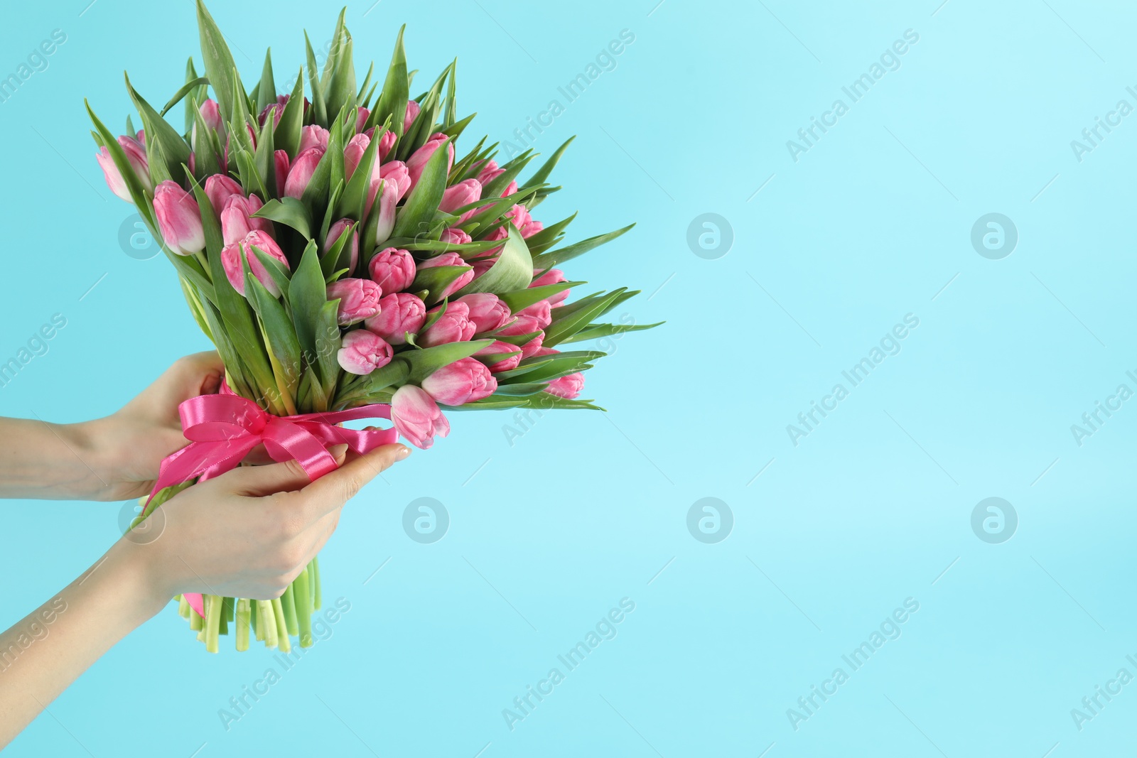 Photo of Woman with bouquet of beautiful tulips on light blue background, closeup. Space for text