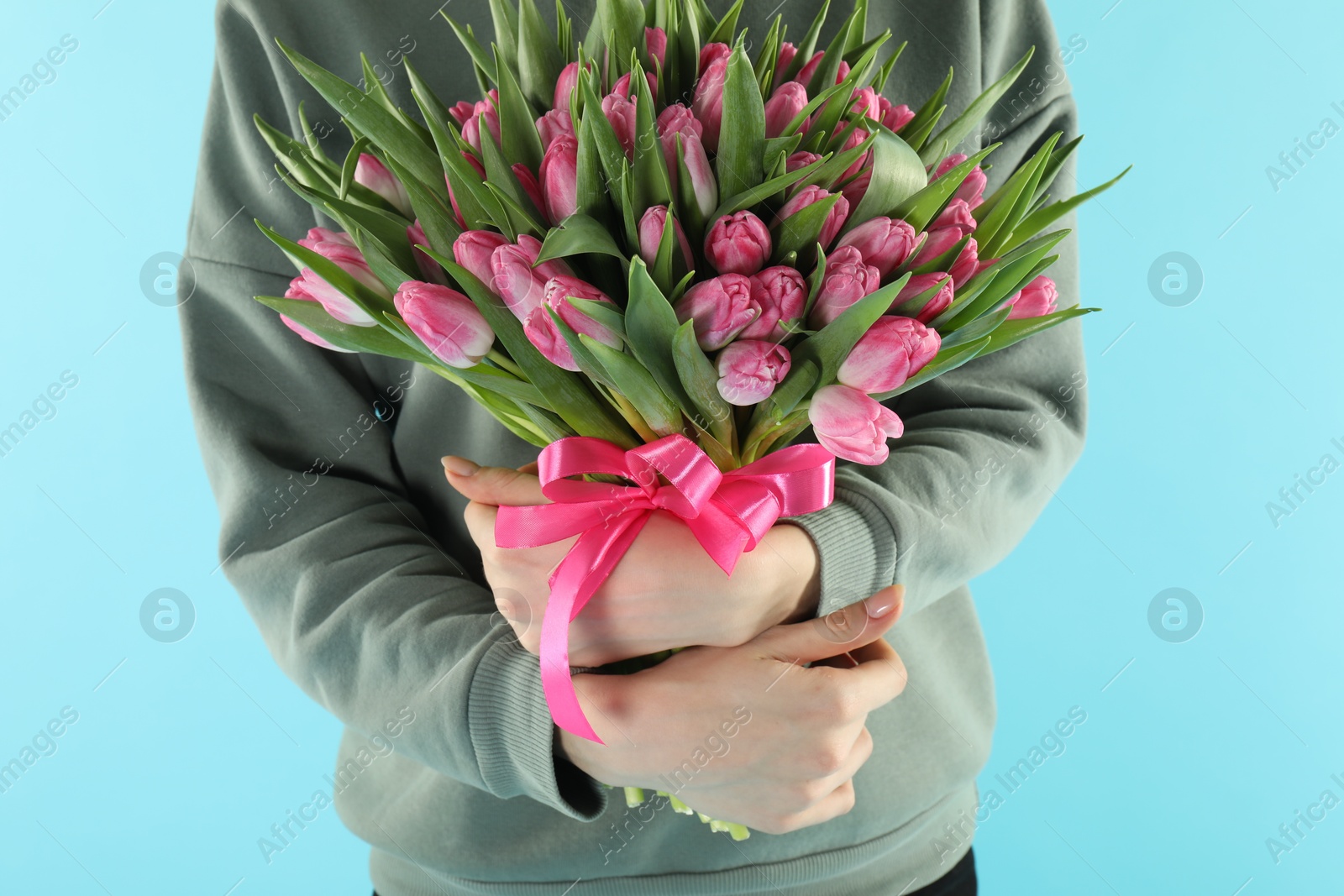 Photo of Woman with bouquet of beautiful tulips on light blue background, closeup