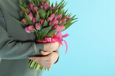 Woman with bouquet of beautiful tulips on light blue background, closeup. Space for text