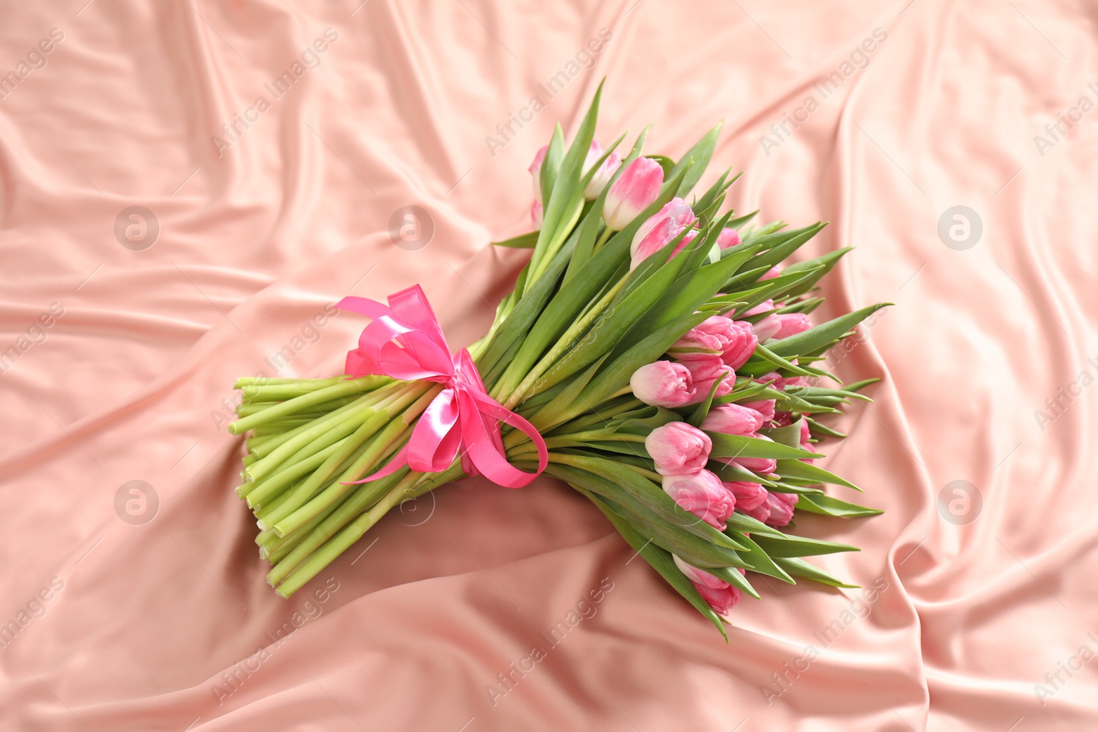 Photo of Bouquet of beautiful tulips on silk fabric, above view