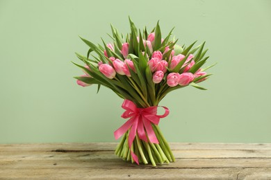 Bouquet of beautiful tulips on wooden table against pale green background