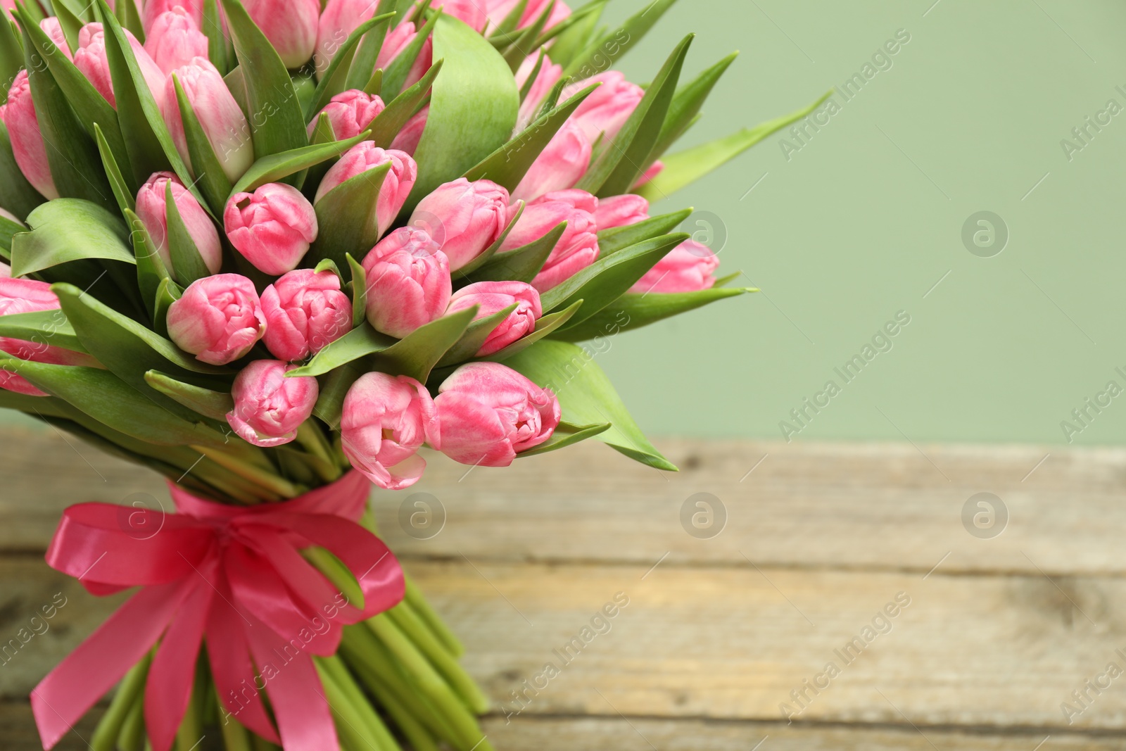 Photo of Bouquet of beautiful tulips on wooden table against pale green background, closeup. Space for text