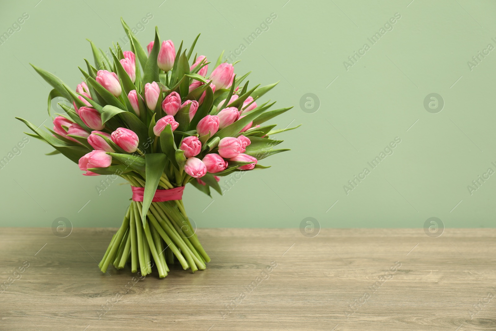 Photo of Bouquet of beautiful tulips on wooden table against pale green background, space for text