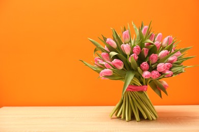 Photo of Bouquet of beautiful tulips on wooden table against orange background, space for text