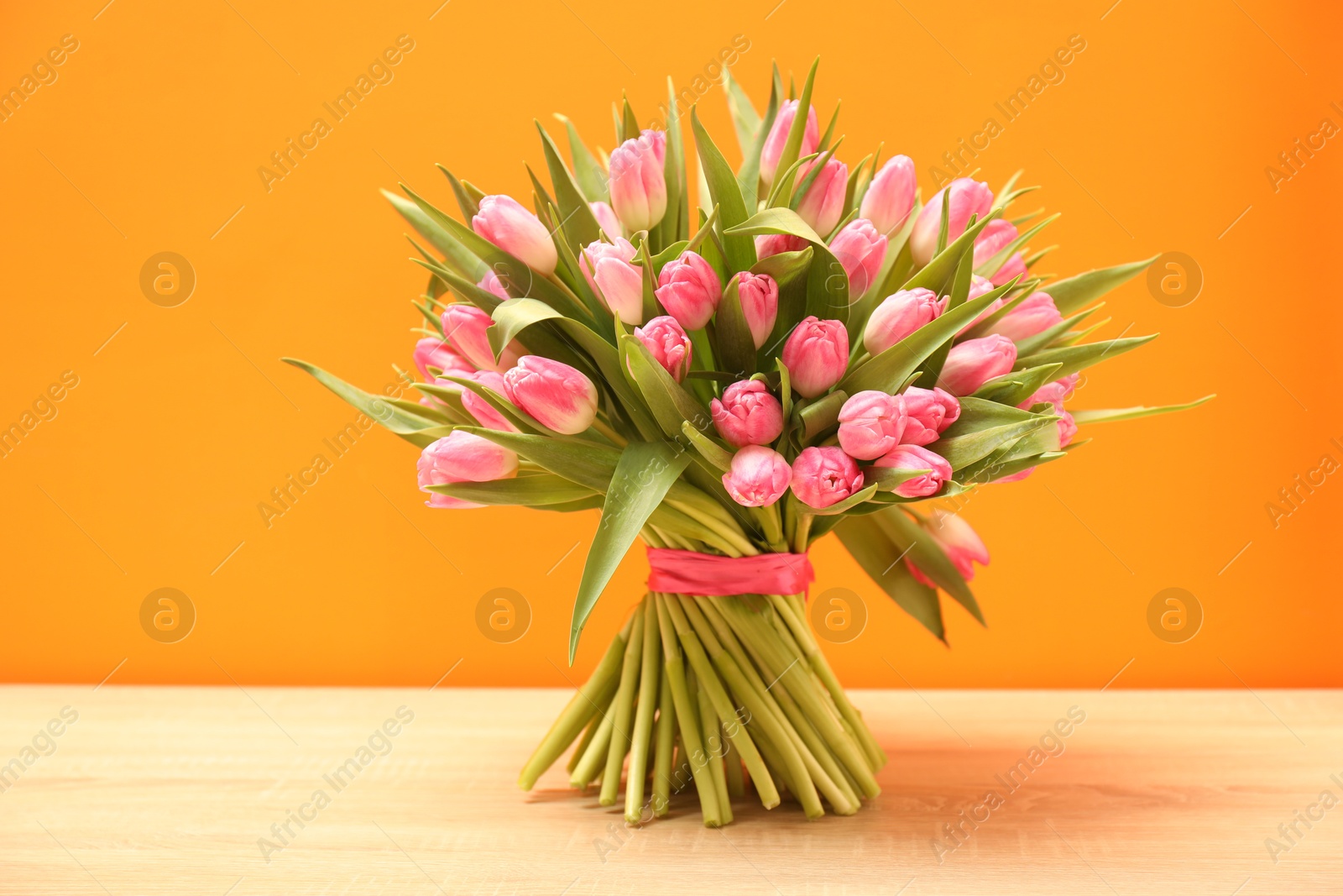 Photo of Bouquet of beautiful tulips on wooden table against orange background