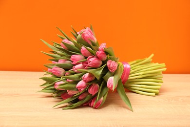 Bouquet of beautiful tulips on wooden table against orange background