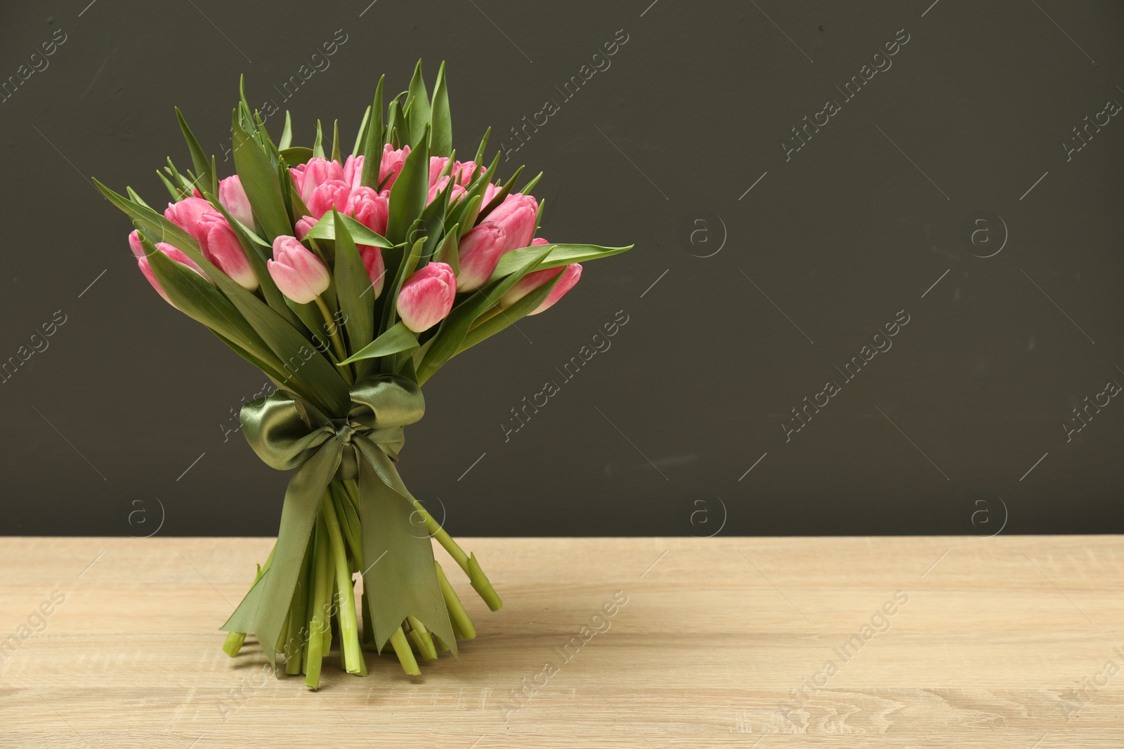 Photo of Bouquet of beautiful tulips on wooden table against grey background, space for text