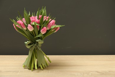 Photo of Bouquet of beautiful tulips on wooden table against grey background, space for text