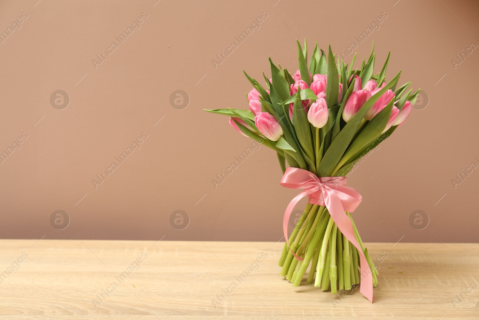 Photo of Bouquet of beautiful tulips on wooden table against dark beige background, space for text