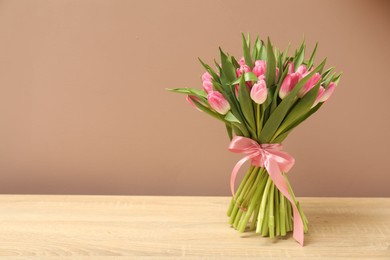 Bouquet of beautiful tulips on wooden table against dark beige background, space for text