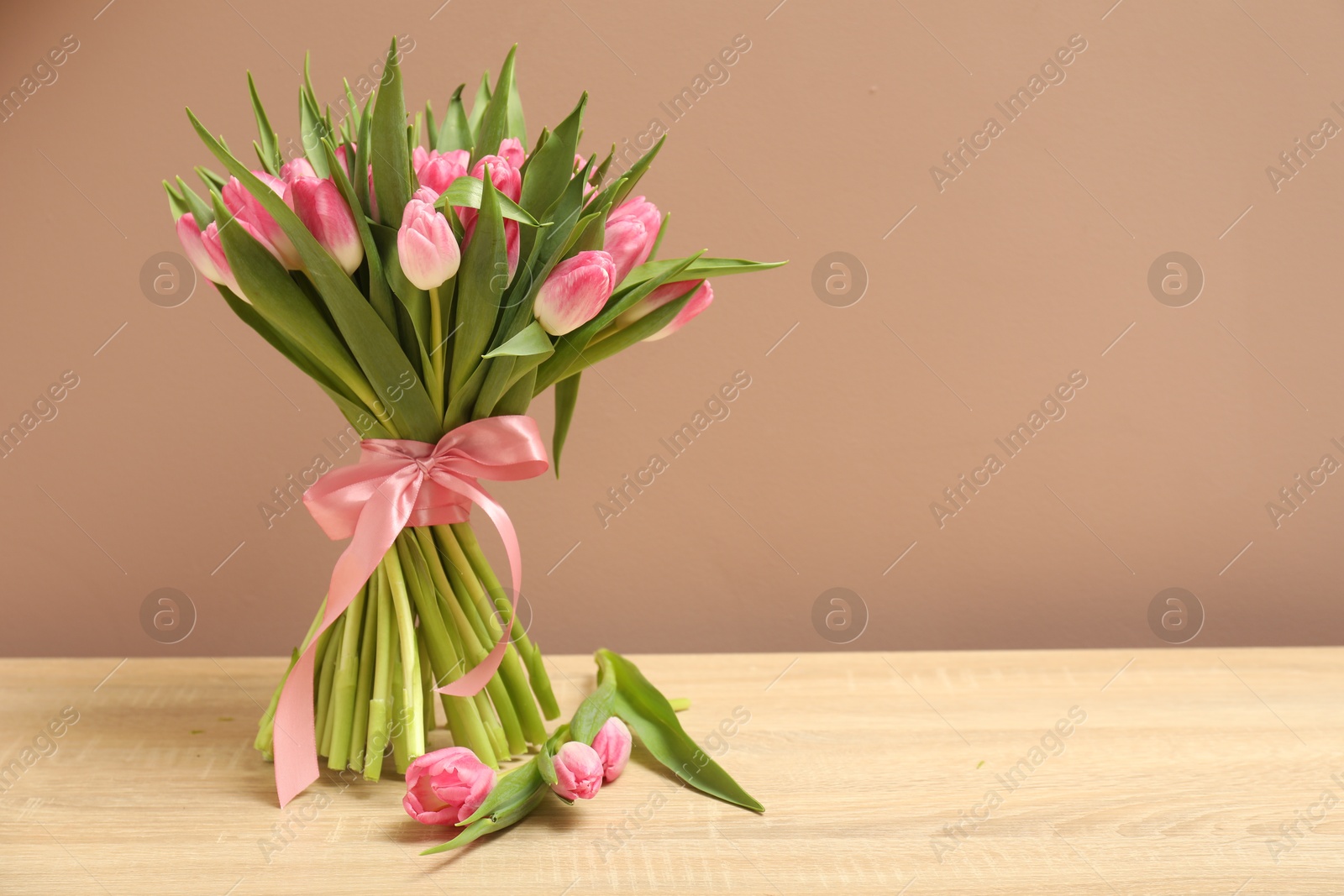 Photo of Bouquet of beautiful tulips on wooden table against dark beige background, space for text