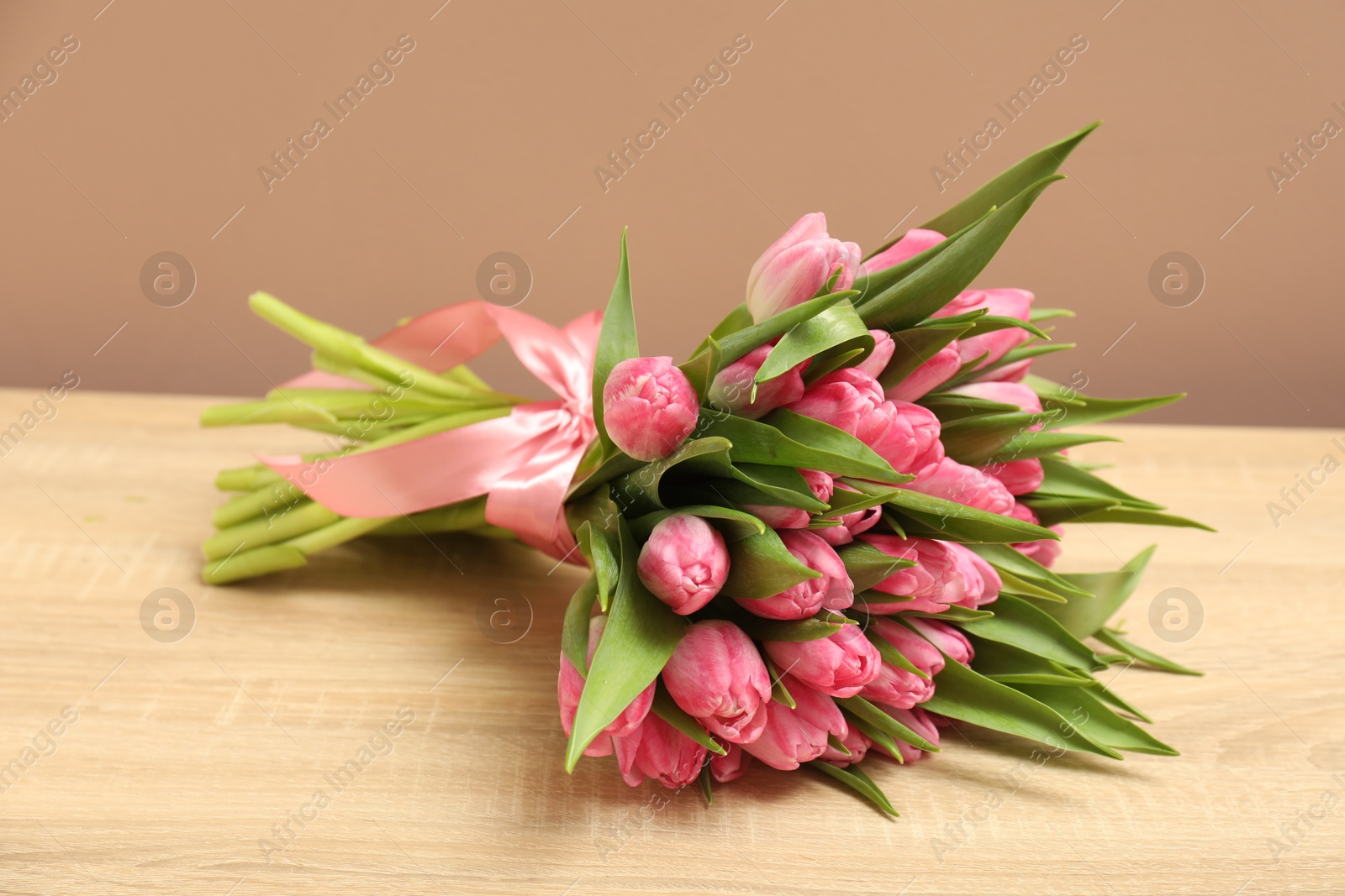 Photo of Bouquet of beautiful tulips on wooden table against dark beige background, closeup