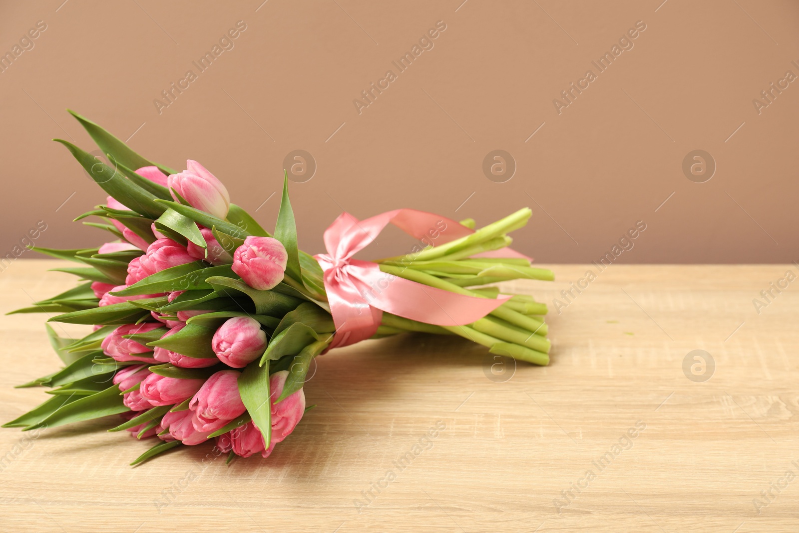 Photo of Bouquet of beautiful tulips on wooden table against dark beige background, space for text