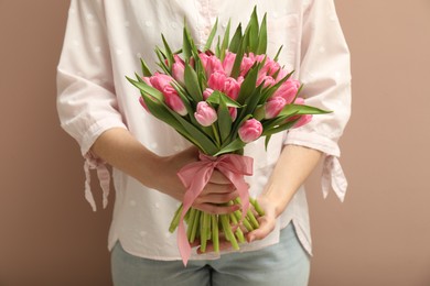 Photo of Woman with bouquet of beautiful tulips on dark beige background, closeup