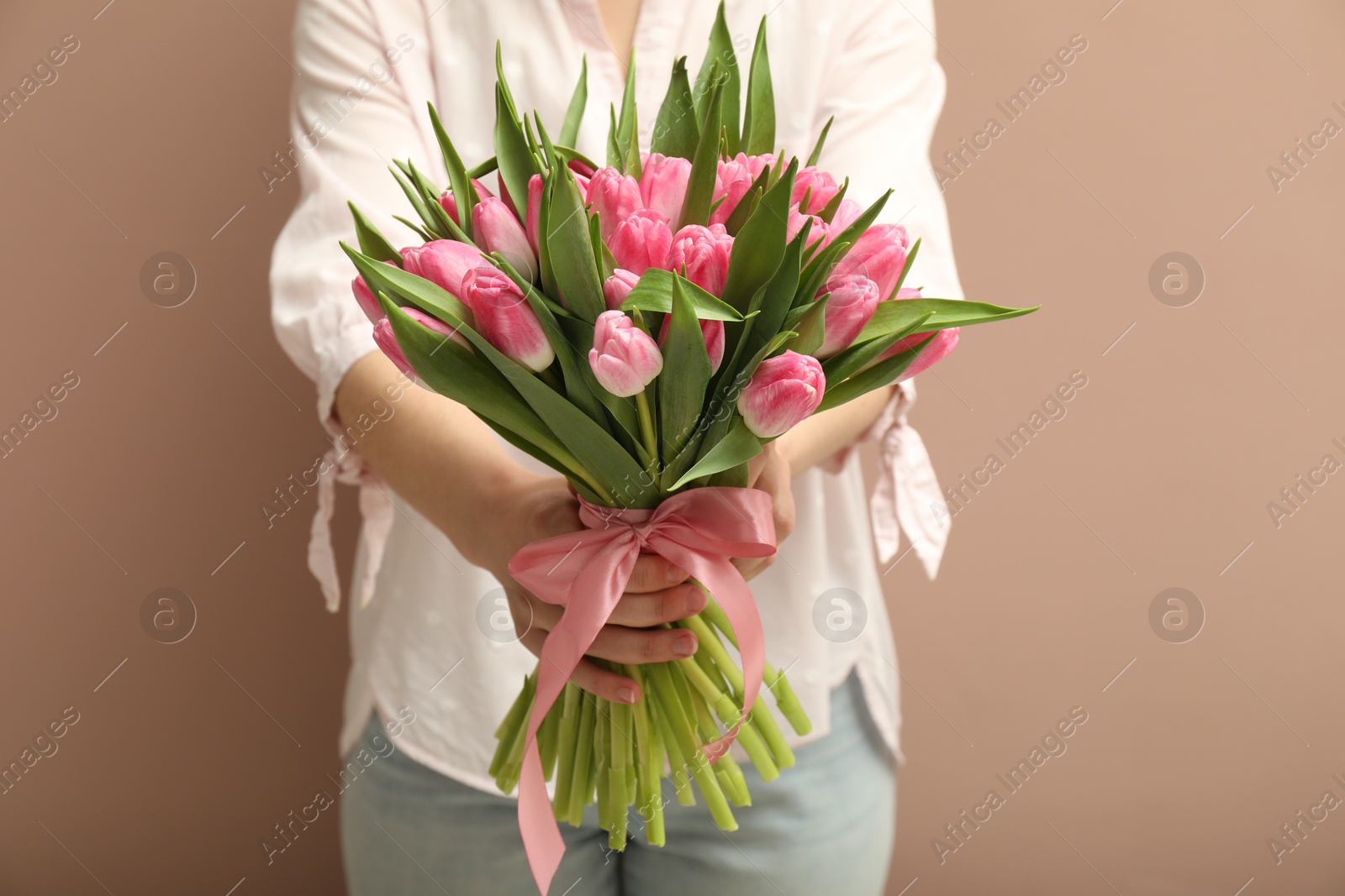 Photo of Woman with bouquet of beautiful tulips on dark beige background, closeup