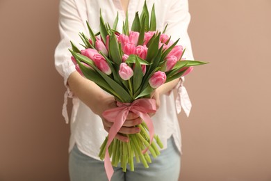 Woman with bouquet of beautiful tulips on dark beige background, closeup