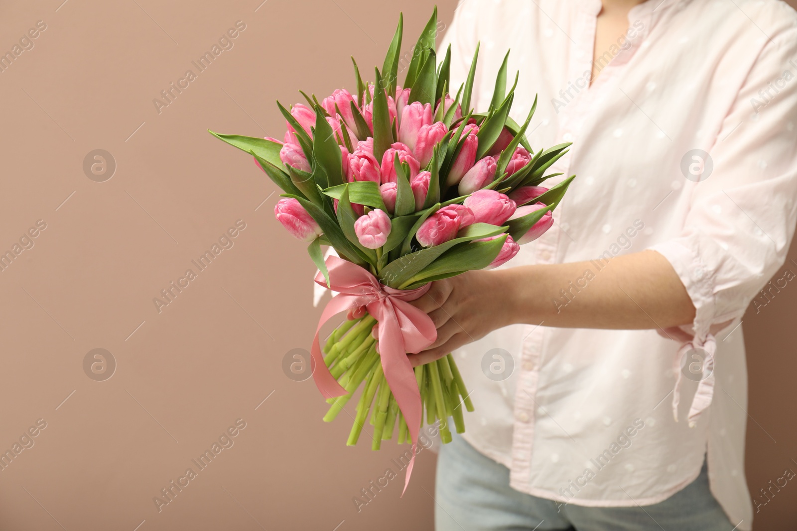 Photo of Woman with bouquet of beautiful tulips on dark beige background, closeup. Space for text