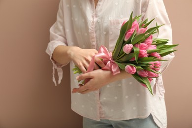 Photo of Woman with bouquet of beautiful tulips on dark beige background, closeup. Space for text