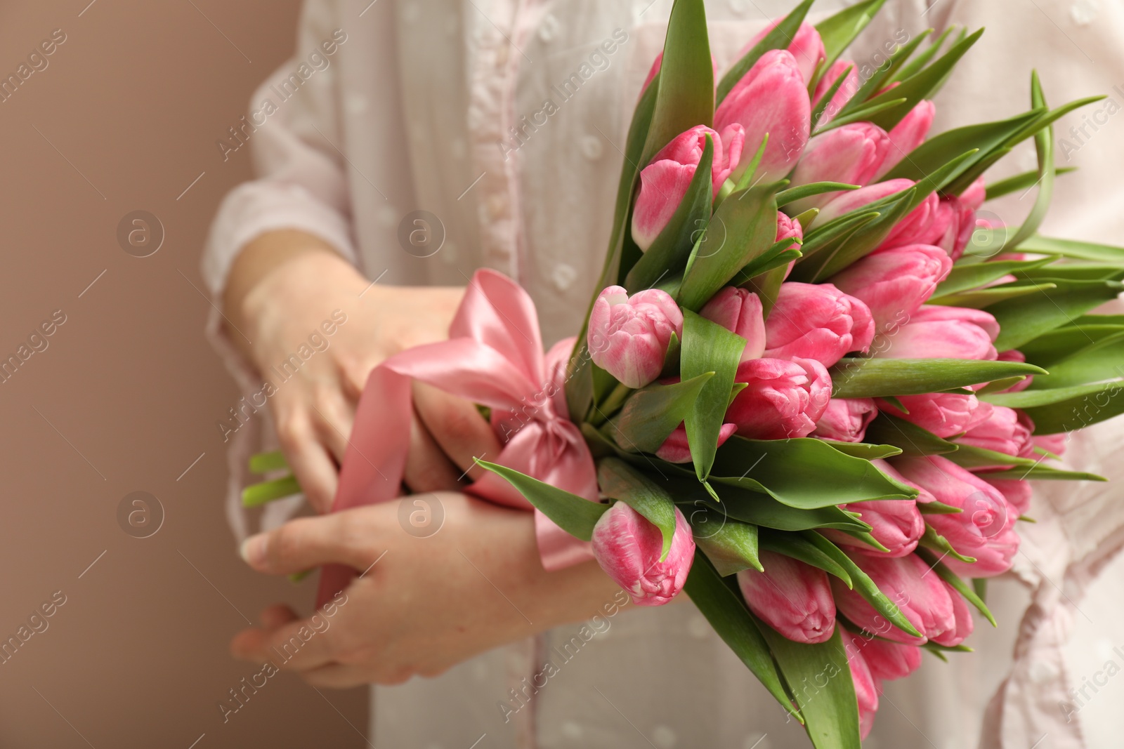 Photo of Woman with bouquet of beautiful tulips on dark beige background, closeup